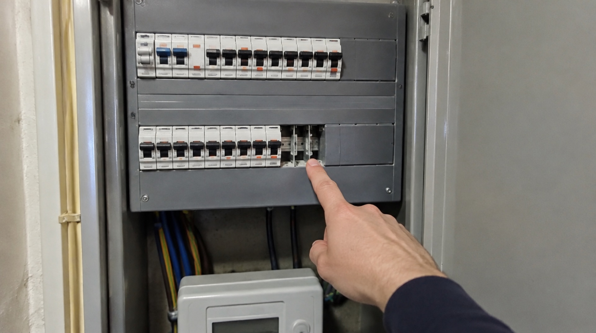 Hand wijst naar een lege plek in een geopende groepenkast met automaten in de meterkast