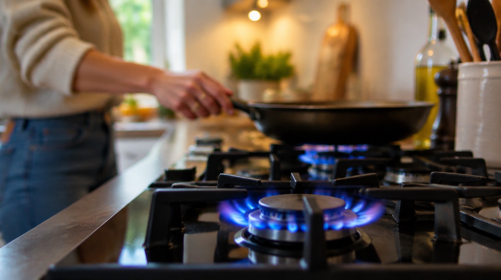 Blauwe gasvlammen op een kookplaat terwijl iemand een pan pakt